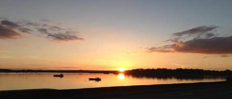 Un atardecer sobre una superficie acuática tranquila con barcos y una costa lejana.