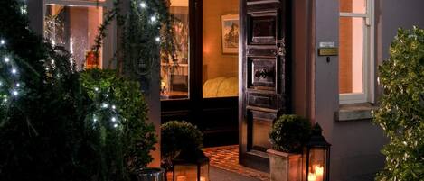 A warmly lit entrance with a dark door, a small seating area with a table and chairs, and a potted plant.