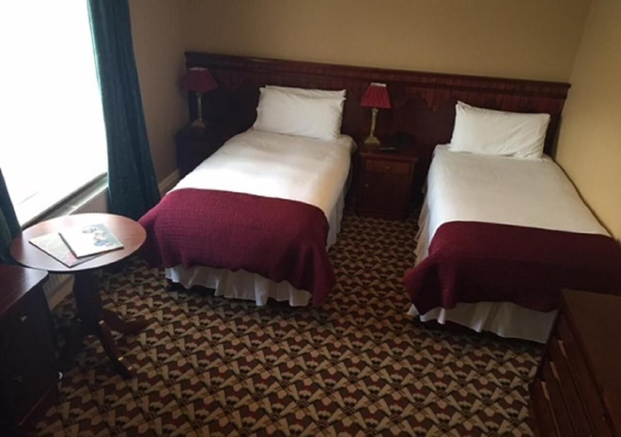 Habitación de hotel con dos camas, una mesita y una alfombra estampada.