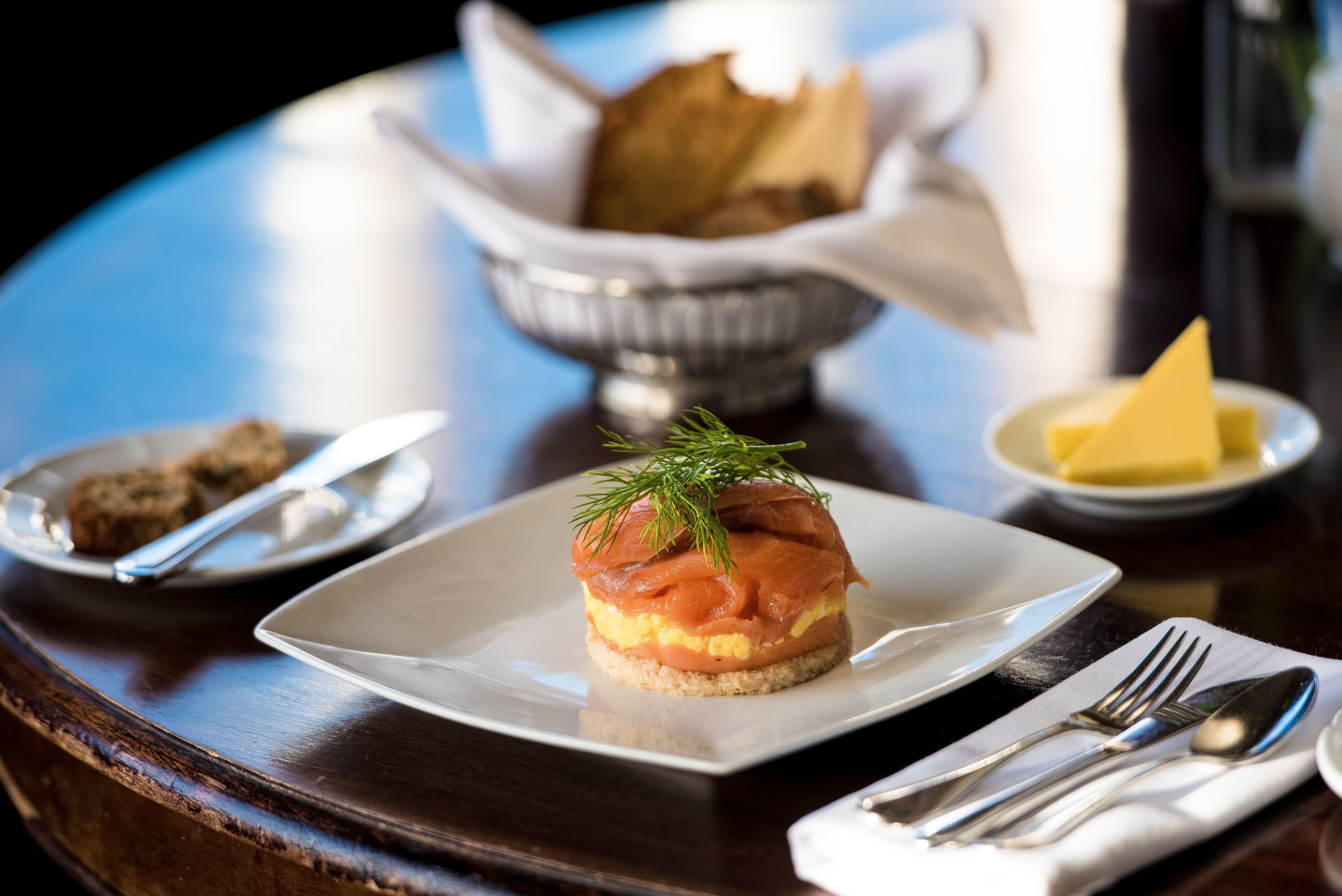 A plate with a sandwich, a bowl of bread, and a small dish of butter on a table.