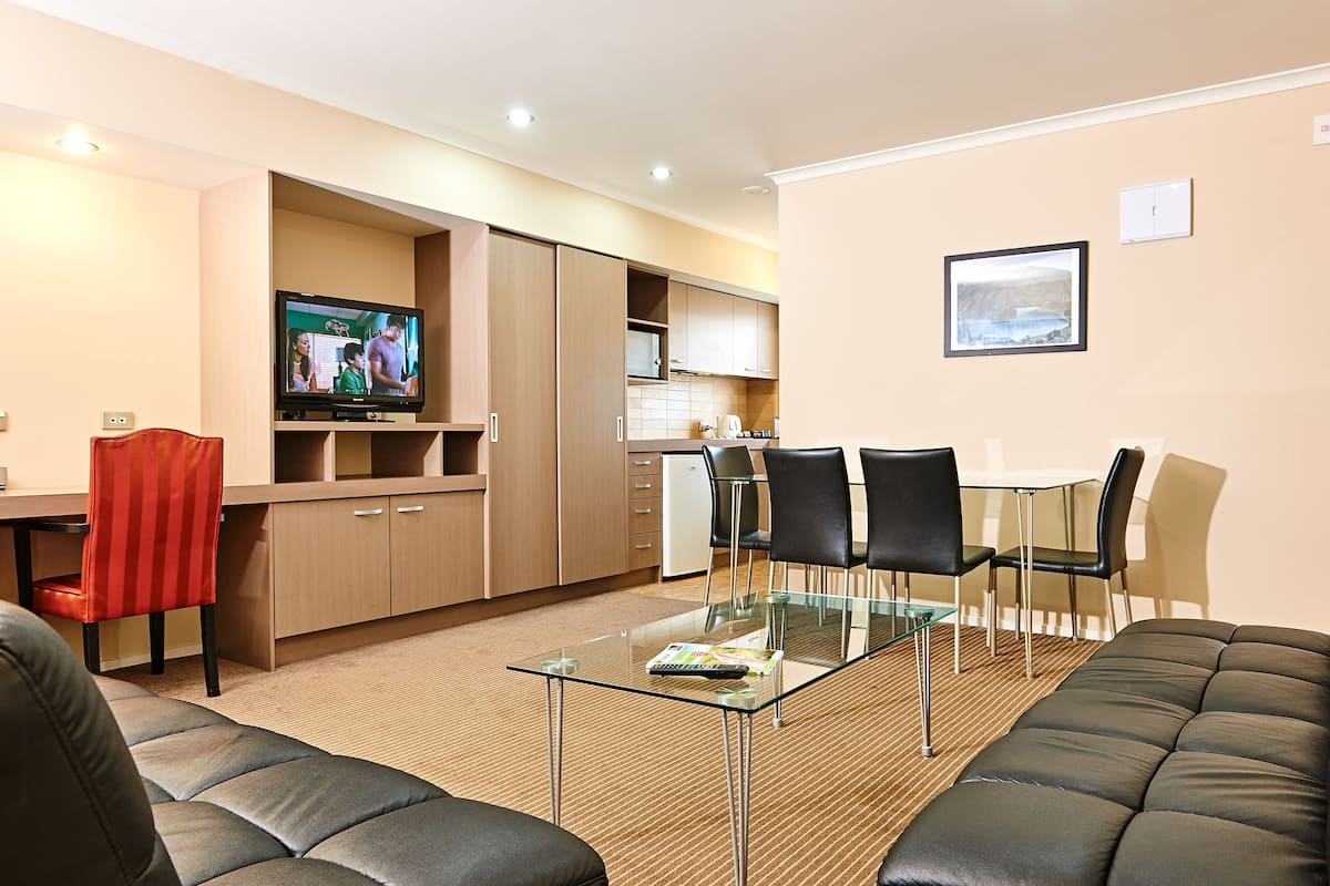Un área de estar moderna con una mesa de centro de vidrio, un sofá de cuero y un televisor.