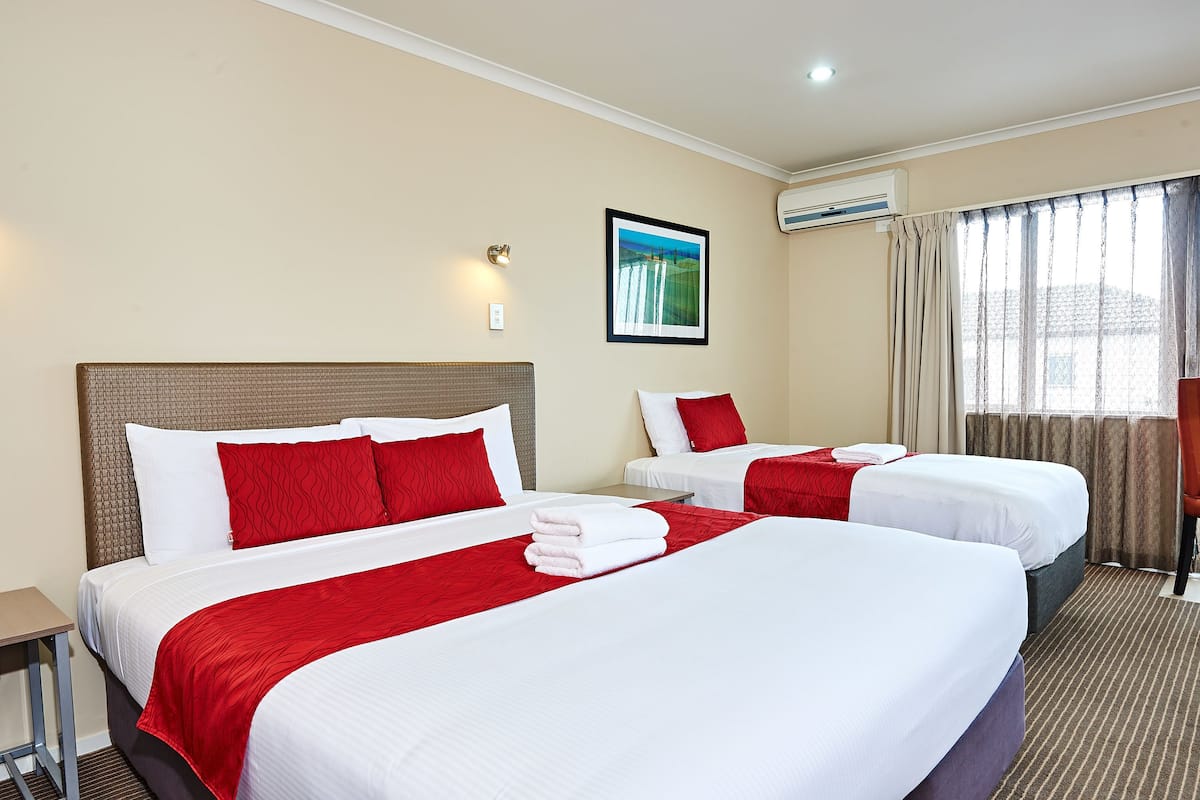 Una habitación de hotel con dos camas, cada una con ropa de cama roja y blanca, una mesita pequeña y un cuadro en la pared.