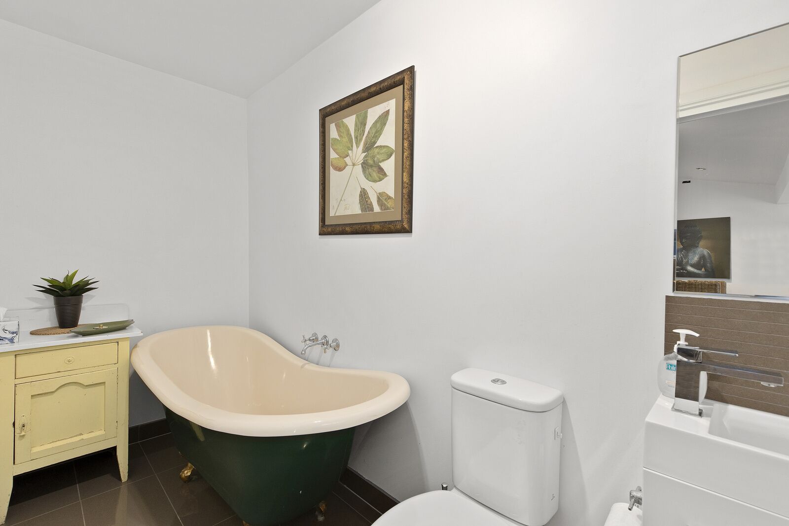 A bathroom with a freestanding bathtub, a toilet, a sink with a mirror, and a framed botanical print on the wall.