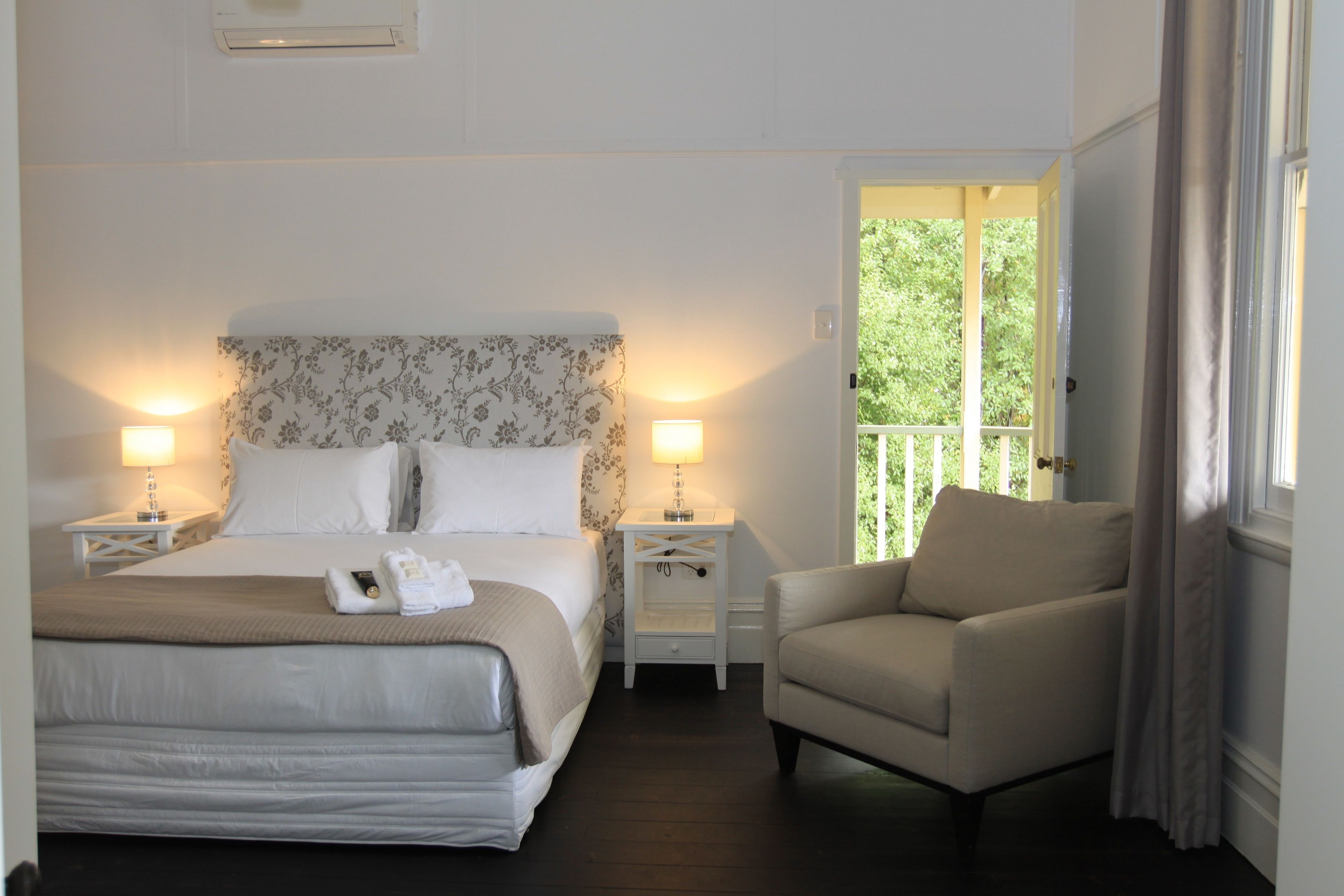 A hotel room with a large bed, two bedside tables with lamps, a chair, and a window with a view of greenery.