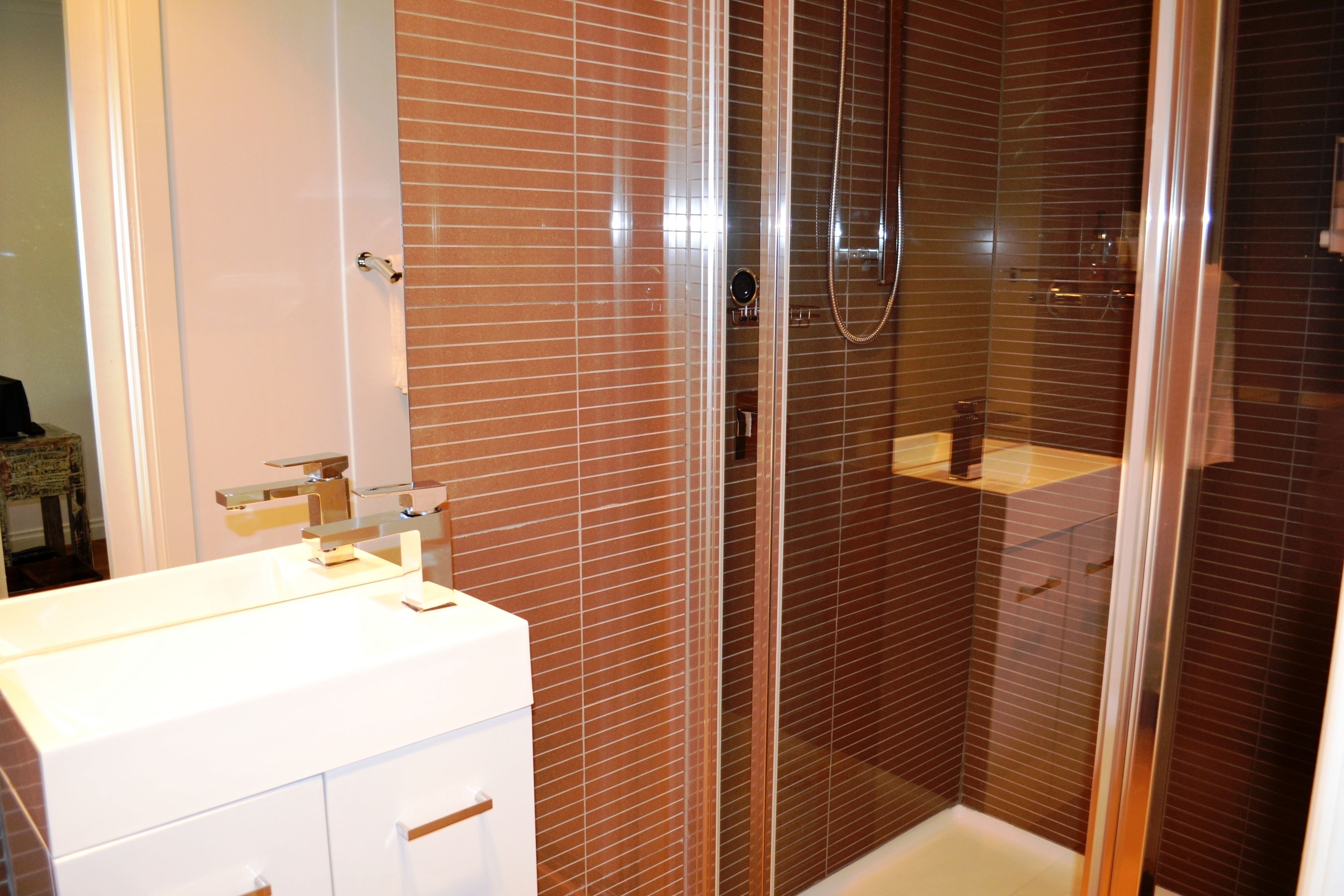 Un baño con un lavamanos blanco, una mampara de cristal para la ducha y paredes con azulejos marrones.