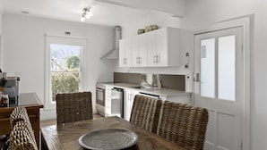 Een moderne keuken met witte kastjes, een eettafel met rieten stoelen en een groot raam met uitzicht op groen.