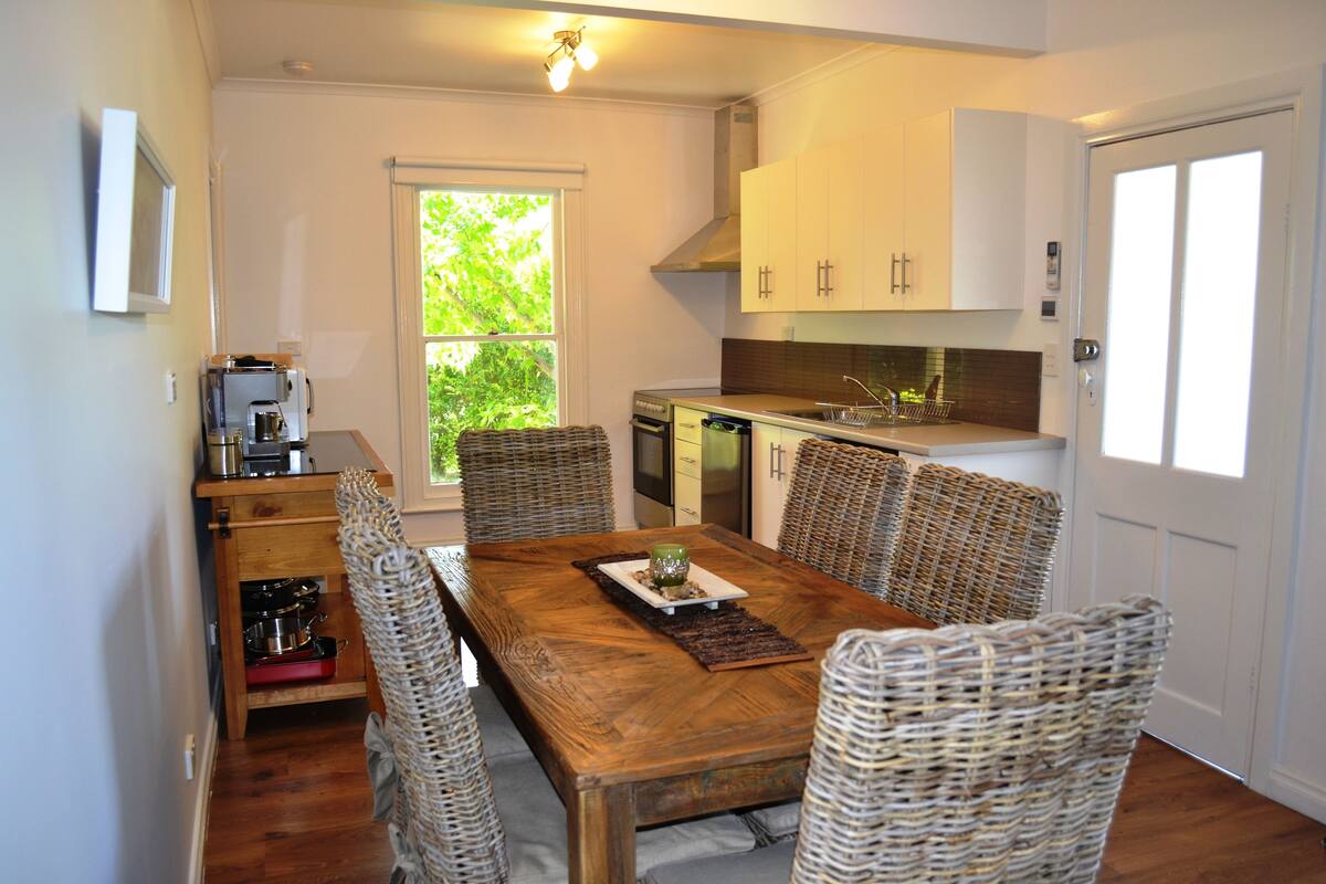 A dining area with a wooden table, wicker chairs, and a view of the outdoors.