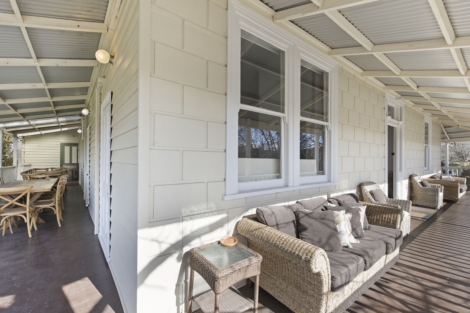 A covered porch with wicker furniture, a table, and a large window.