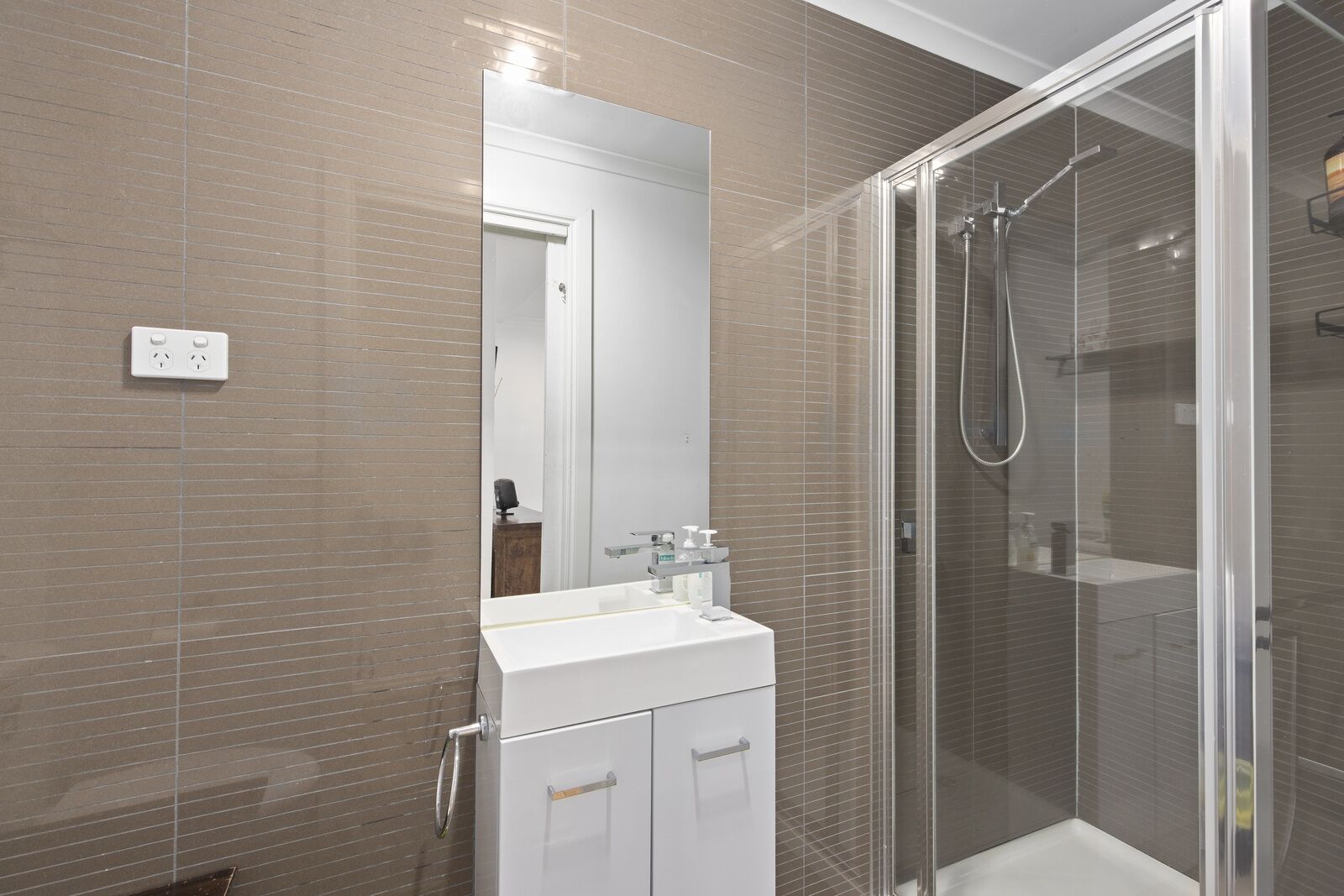 Un bagno moderno con cabina doccia in vetro, lavandino bianco e specchio sopra.