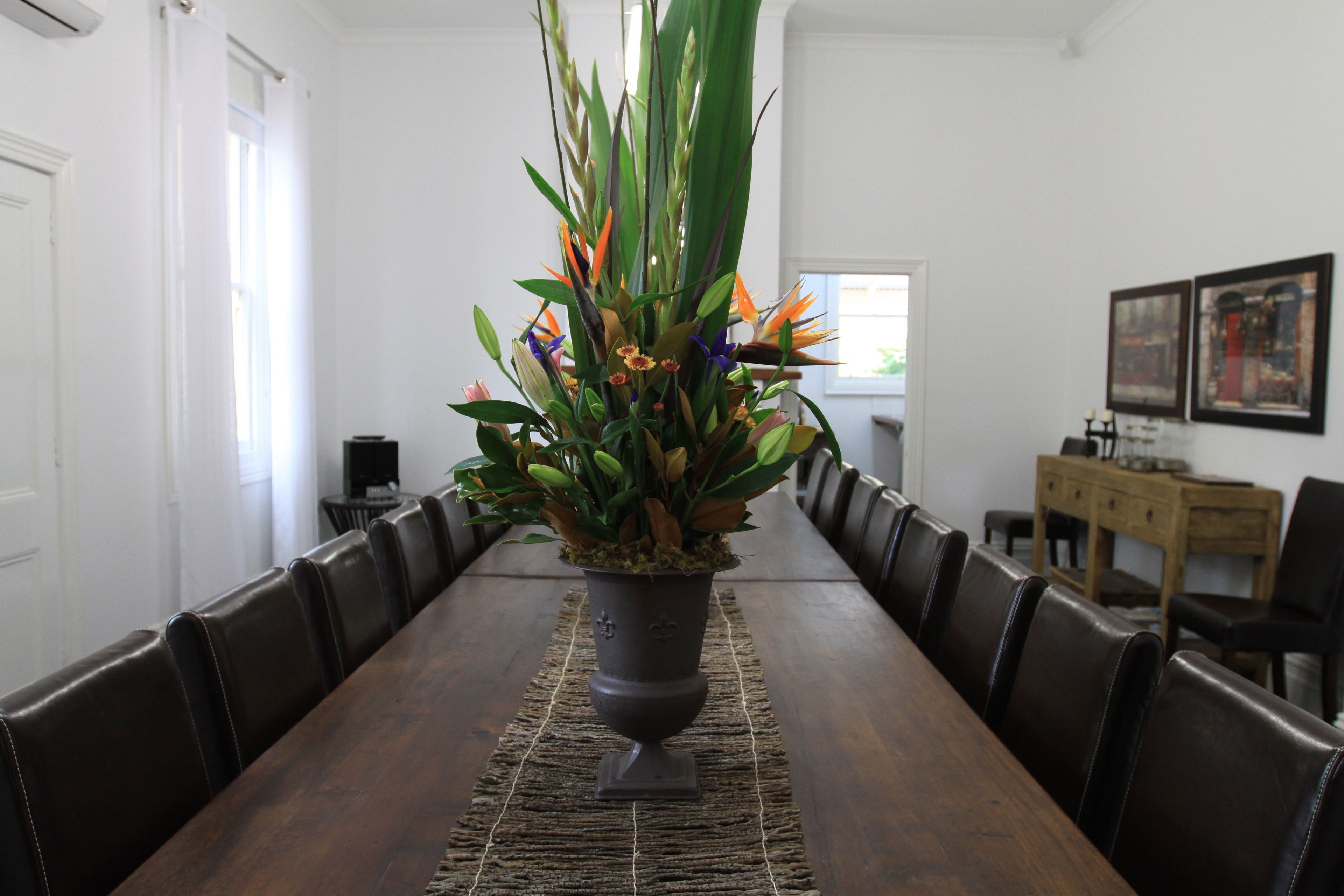 A long wooden dining table with a potted plant in the center, surrounded by leather chairs.