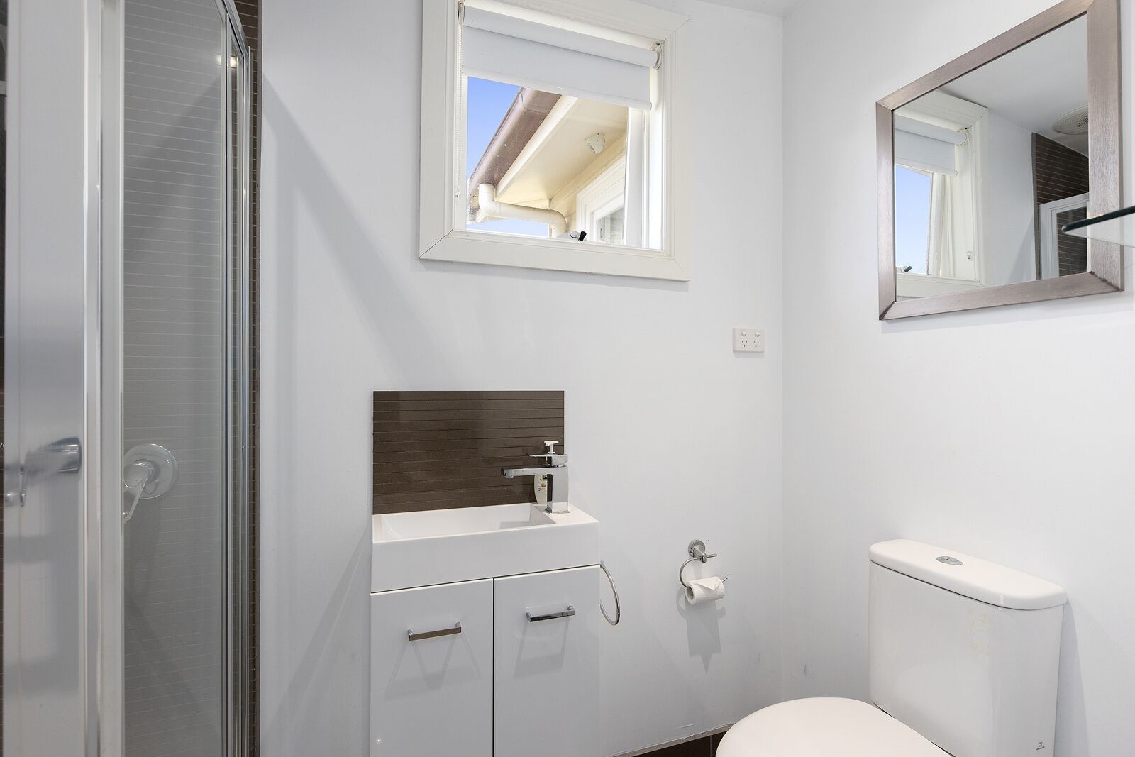Ein modernes Badezimmer mit Duschkabine aus Glas, einem weißen Waschbecken mit Holz-Spritzschutz und einer Toilette.