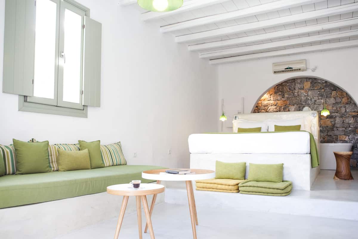 Une pièce moderne et bien éclairée, avec un canapé vert, un lit blanc et une petite table ronde.