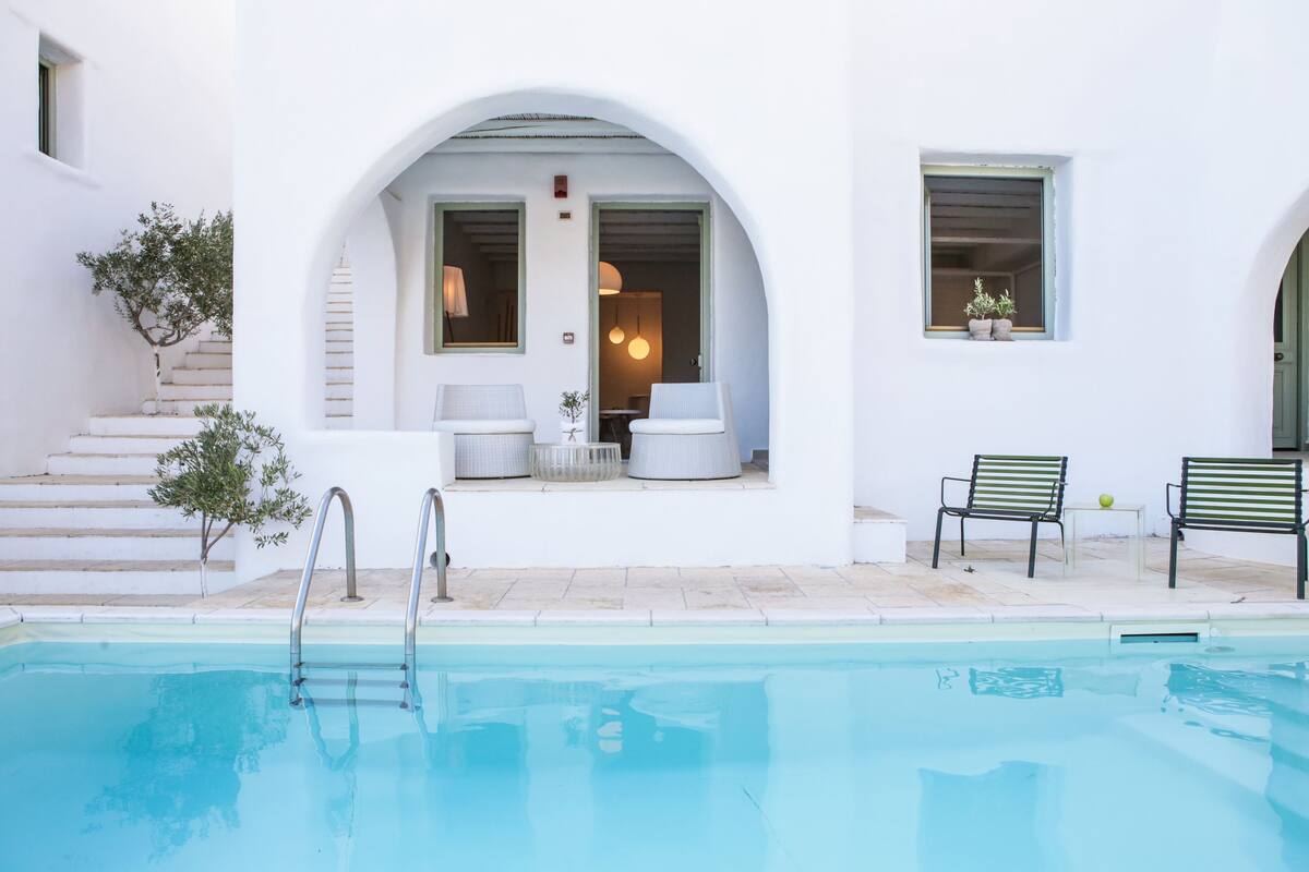 Un espace piscine offrant une vue dégagée sur le bassin, un escalier menant à un espace de repos abrité et une petite table avec des chaises.