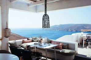 A modern outdoor seating area with a table, chairs, and cushions, overlooking a scenic ocean view. - Pylaia Boutique Hotel & Spa (Astypalaia)