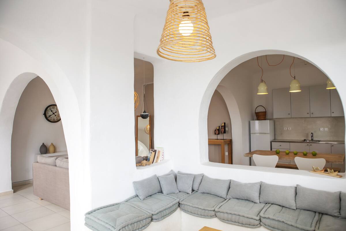 Un salon moderne avec un canapé d’angle, un coin repas doté d’une table en bois et une cuisine visible à travers une arche.