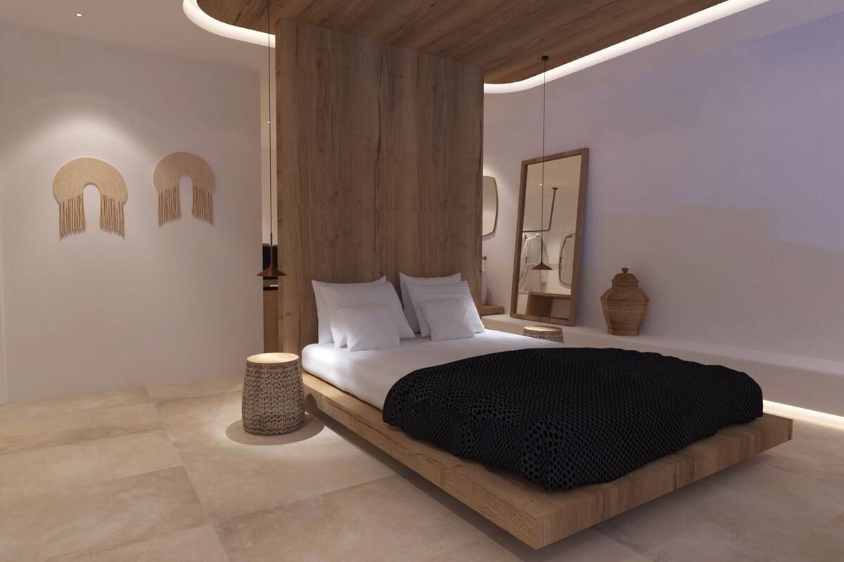Une chambre à coucher moderne avec un lit surélevé en bois, une table d’appoint ronde, un tabouret en osier et un grand miroir.