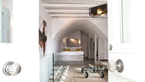 A modern hotel room with a glass staircase, a bed with a yellow accent, and a cart with toiletries. - Pylaia Boutique Hotel & Spa (Astypalaia)