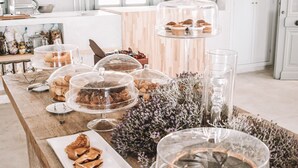 A long wooden table with various food items and glassware, set in a bright kitchen with white cabinets and a clock on the wall. - Pylaia Boutique Hotel & Spa (Astypalaia)