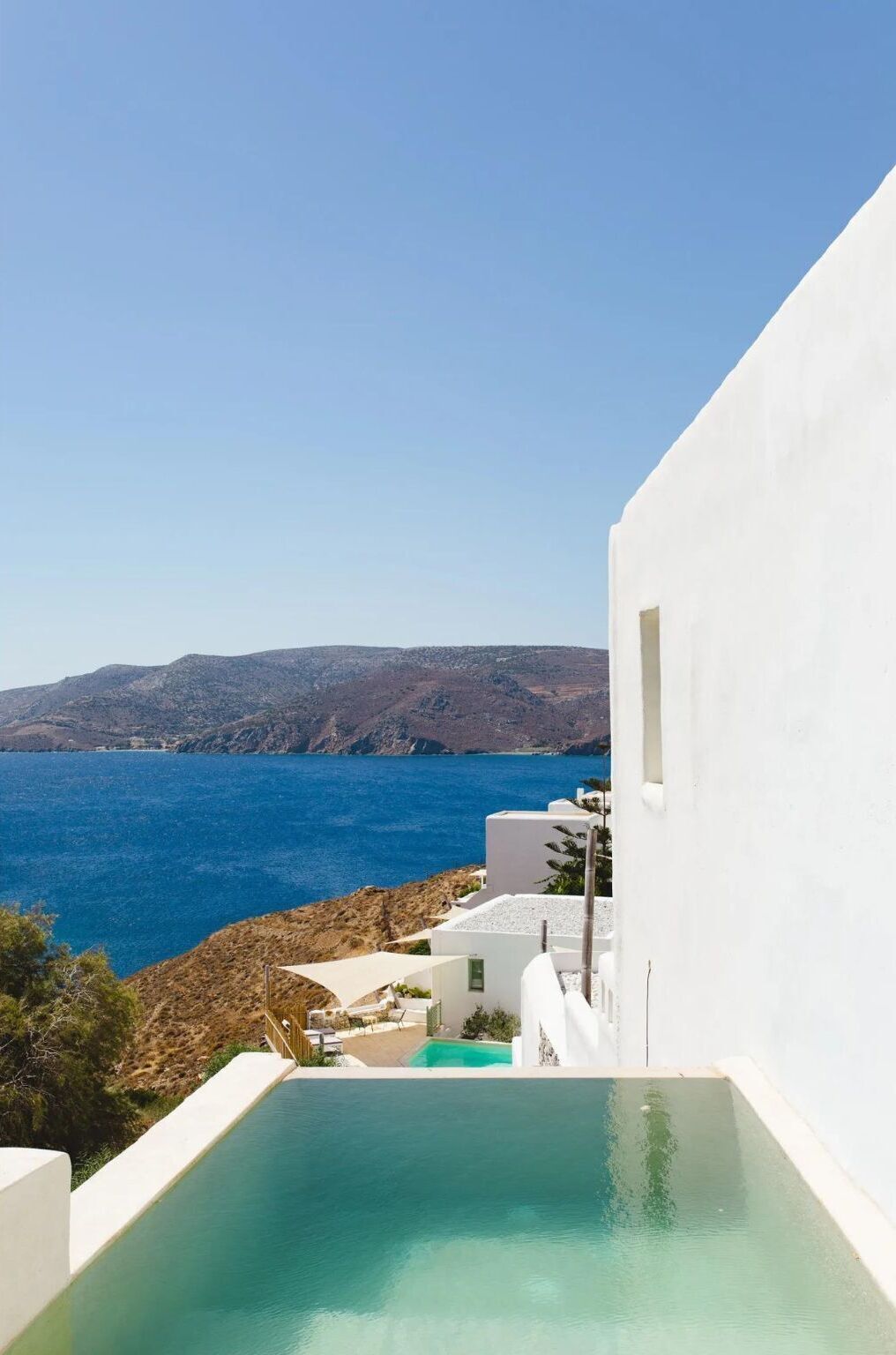 A white building with a pool and a view of the sea.