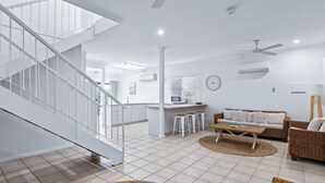 A modern living room with a staircase, a kitchen area, and a dining space. - Cable Beachside Villas (Cable Beach)