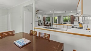A modern kitchen with a central island, a dining area with a wooden table and chairs, and a staircase leading to an upper level. - Cable Beachside Villas (Cable Beach)