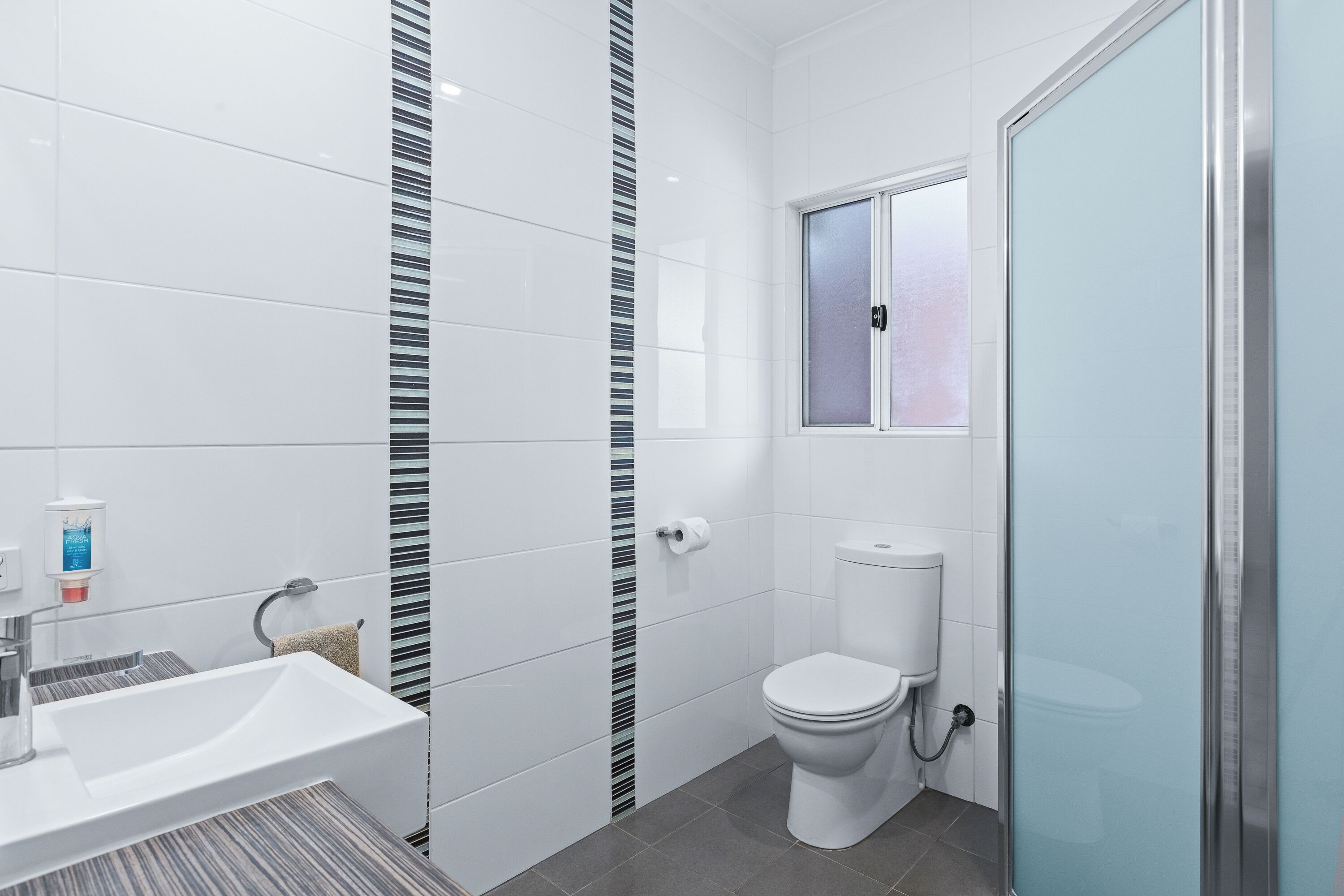 A modern bathroom with a white sink, toilet, and shower area.