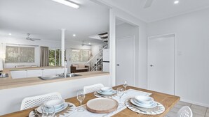A modern kitchen with white cabinets, a wooden countertop, and a dining area with a wooden table set for four. - Cable Beachside Villas (Cable Beach)