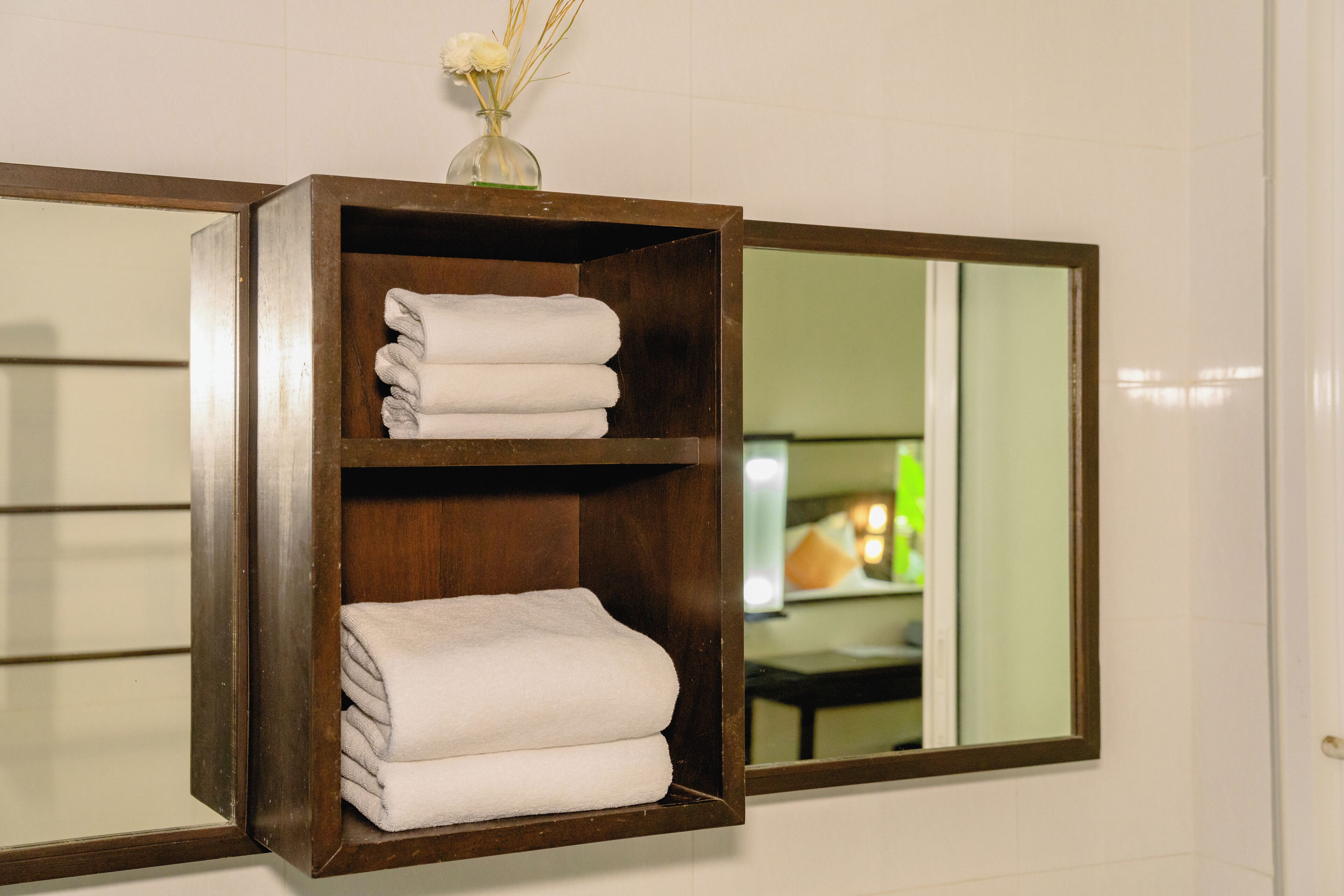 A wooden shelf with folded towels and a vase with dried plants.