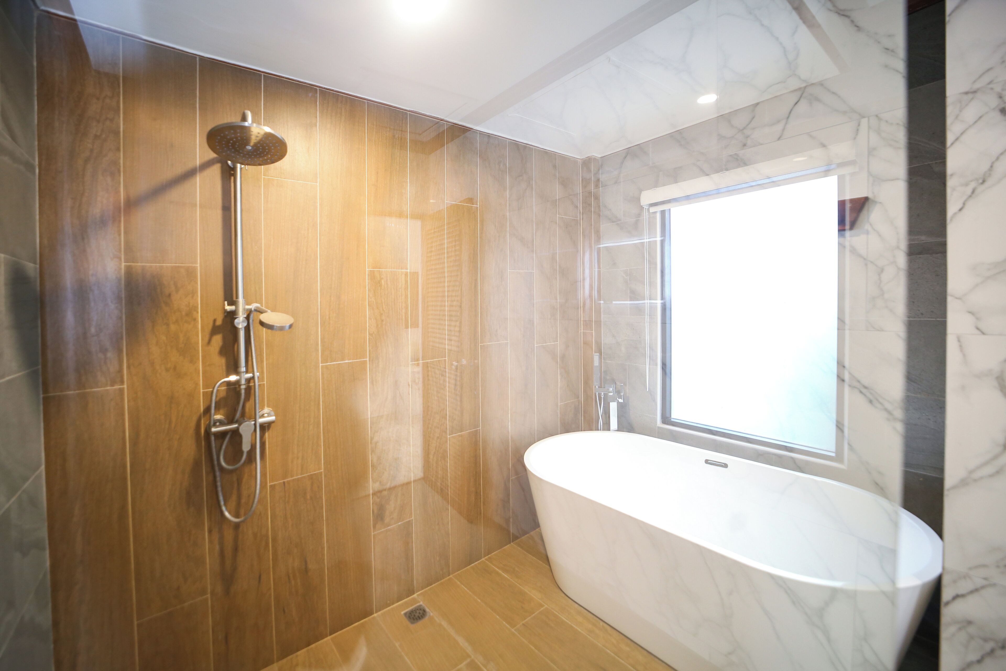 A modern bathroom with a freestanding bathtub, a shower with a handheld showerhead, and a window providing natural light.