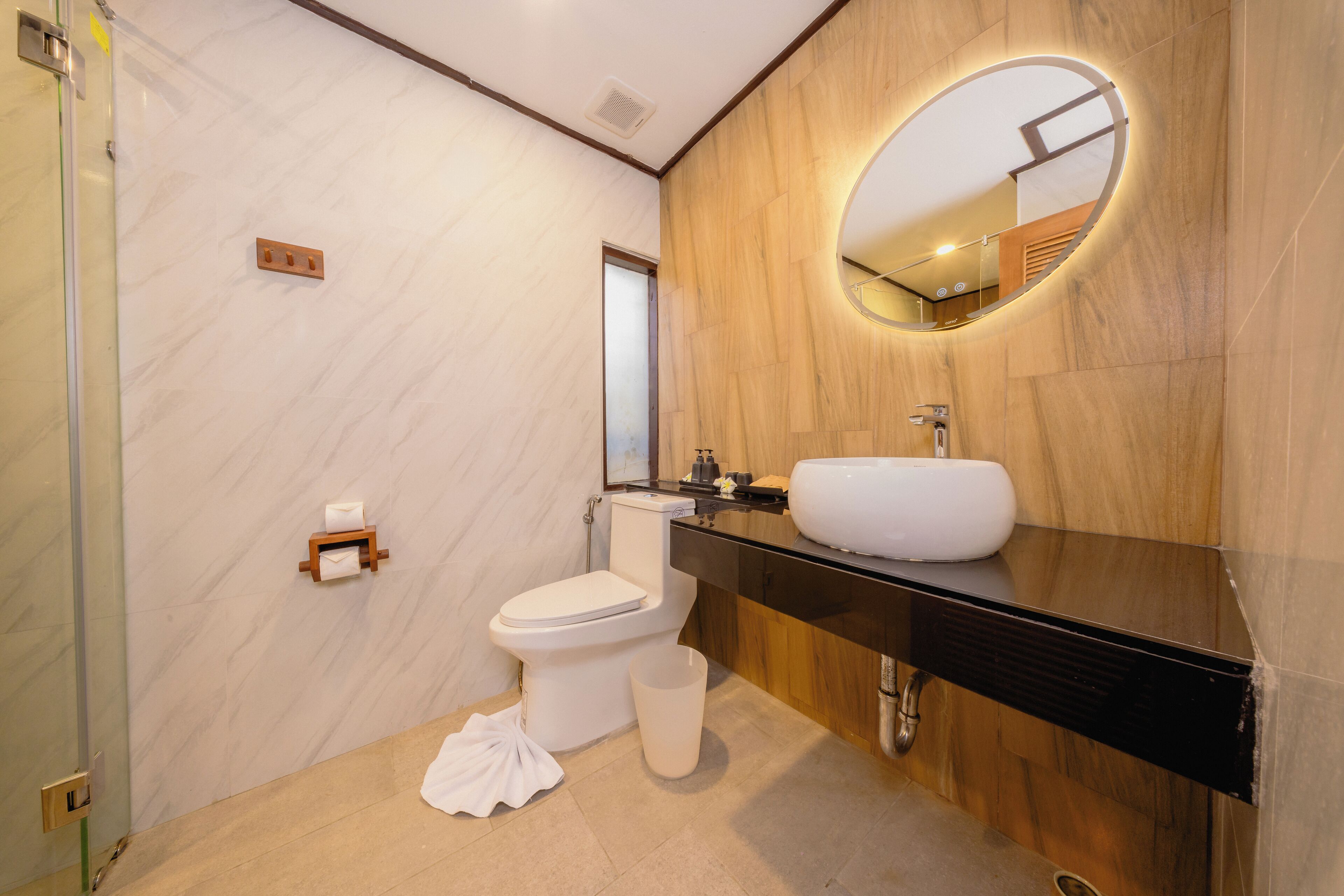 Een moderne badkamer met een marmeren wand, een houten wastafelmeubel, een witte wasbak en een toilet.
