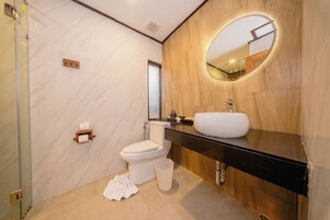 Een moderne badkamer met een marmeren wand, een houten wastafelmeubel, een witte wasbak en een toilet.