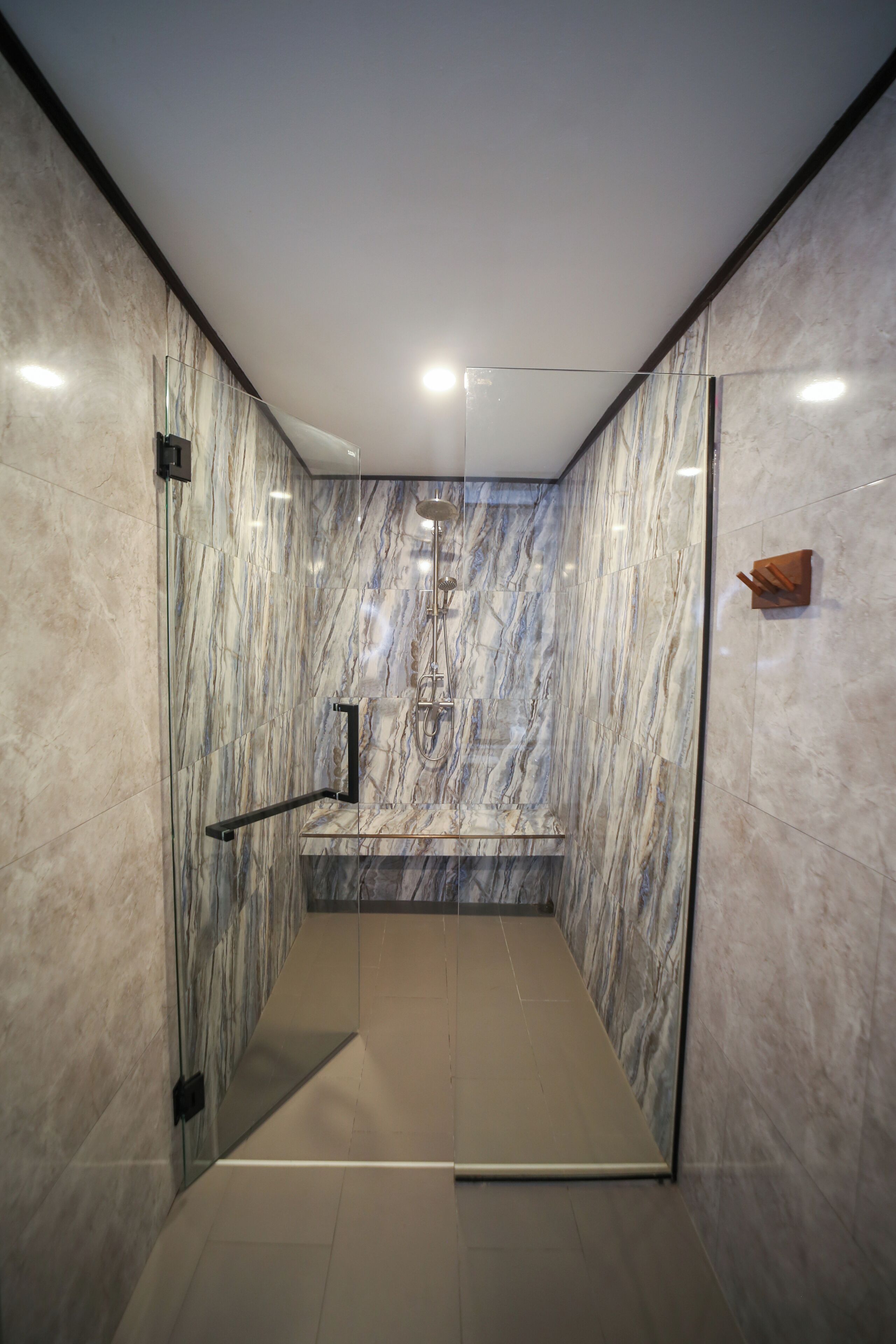 A modern shower area with marble walls and a glass door.