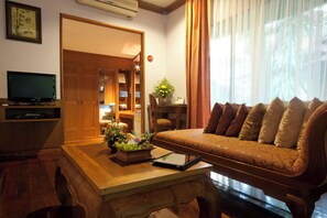 A living room with a sofa, a coffee table with a book and a flower arrangement, a television, and a wooden cabinet.