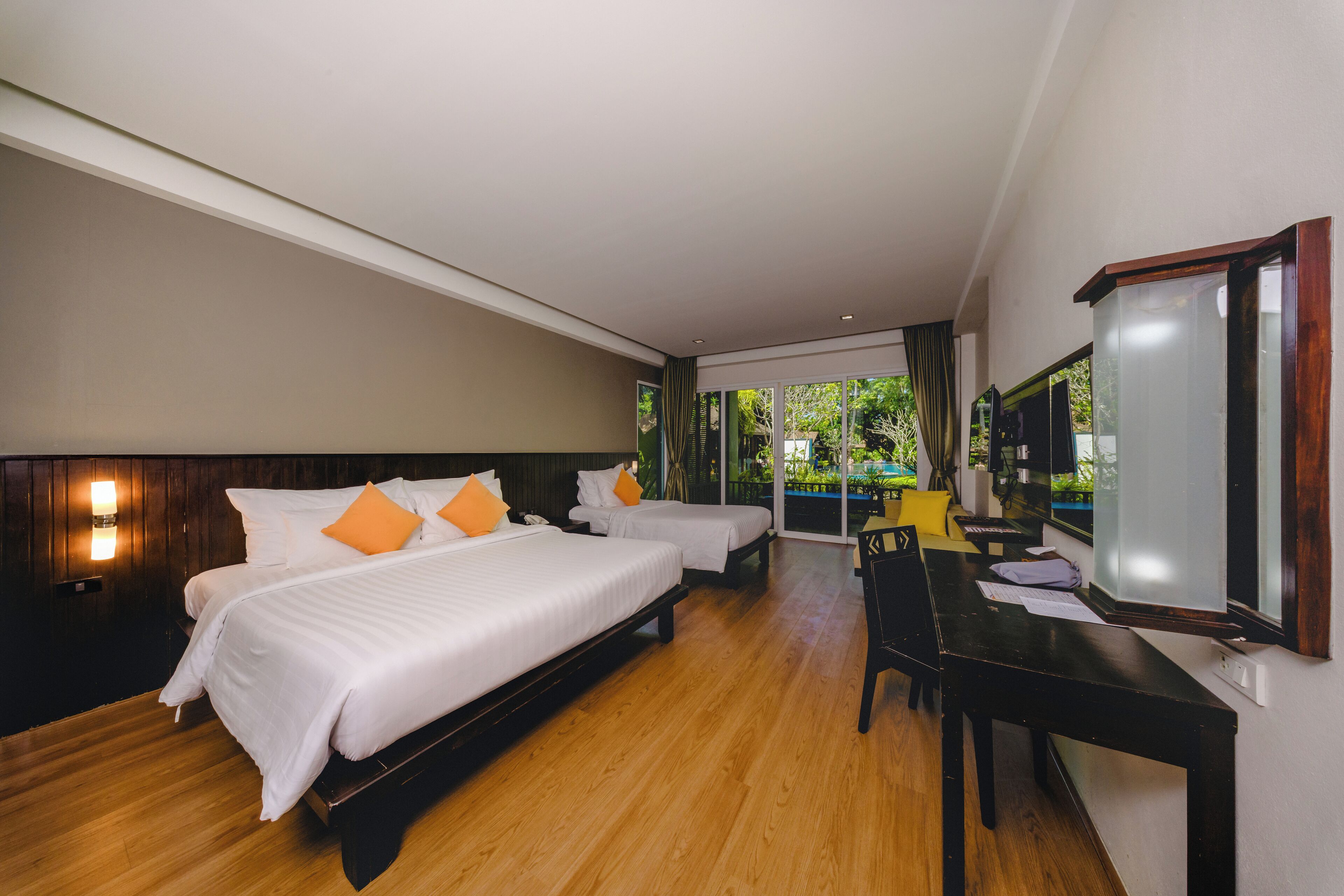 A hotel room with two beds, a desk, and a large window offering a view of greenery.