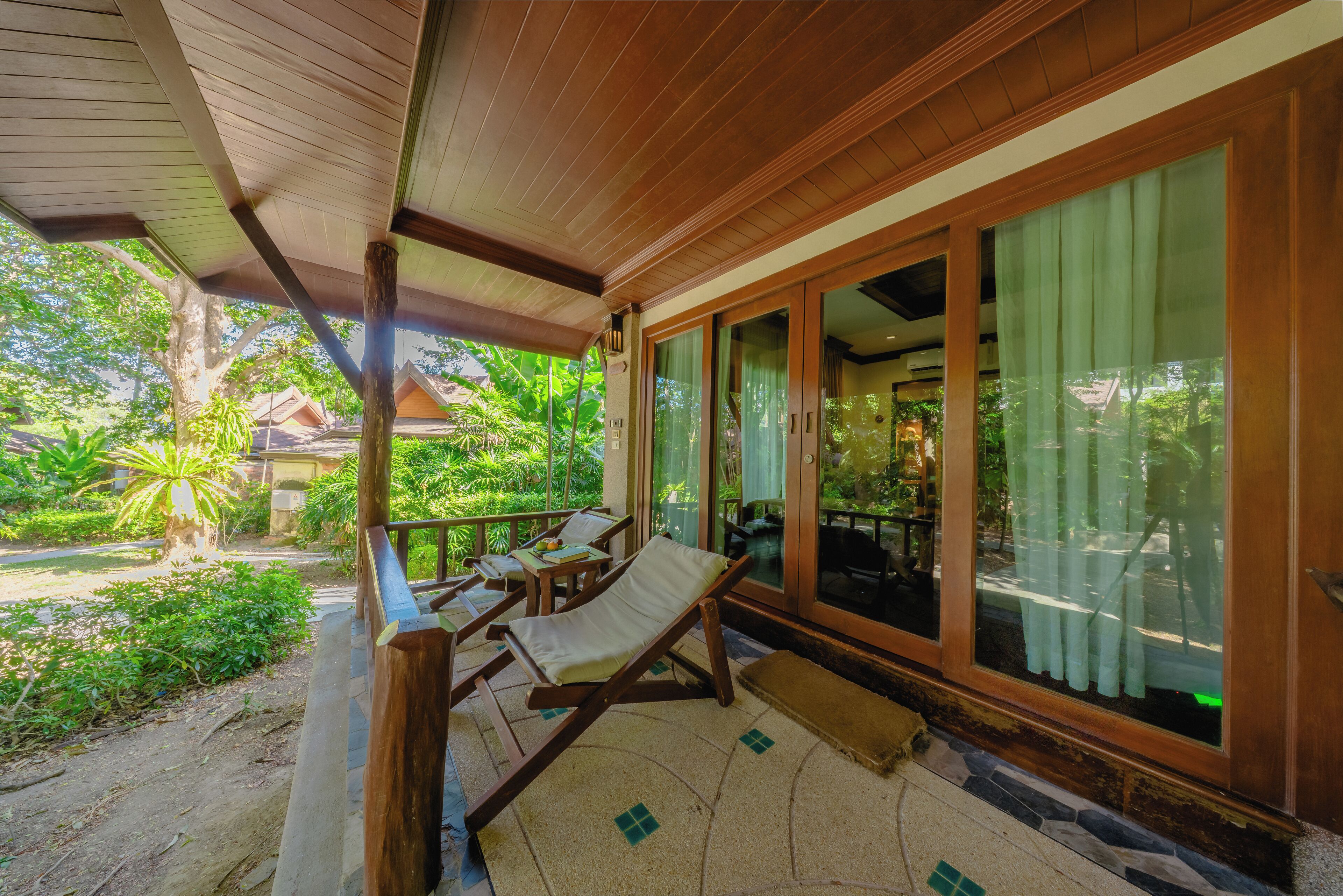 A covered outdoor seating area with wooden furniture and large windows.