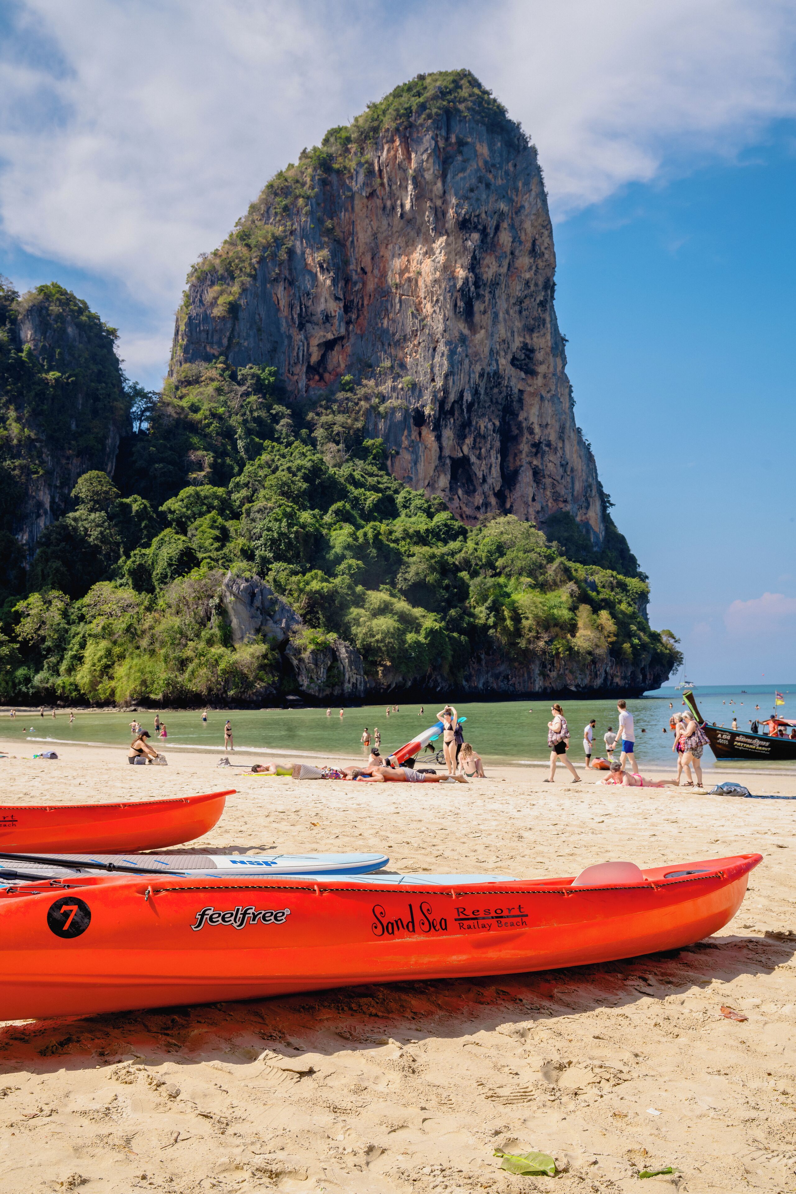A beach with kayaks, a large rock formation, and people enjoying the area.
