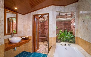 A bathroom with a large bathtub, a sink, and a shower area with a brick wall.