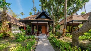 A traditional house with a thatched roof, surrounded by lush greenery and palm trees. - Sand Sea Resort (Krabi)