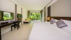 A hotel room with a bed, a desk, a chair, a television, and a balcony with a view of greenery. - Sand Sea Resort (Krabi)