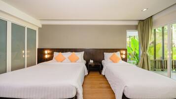 A hotel room with two beds, wooden flooring, a nightstand, and a view of greenery through large windows.