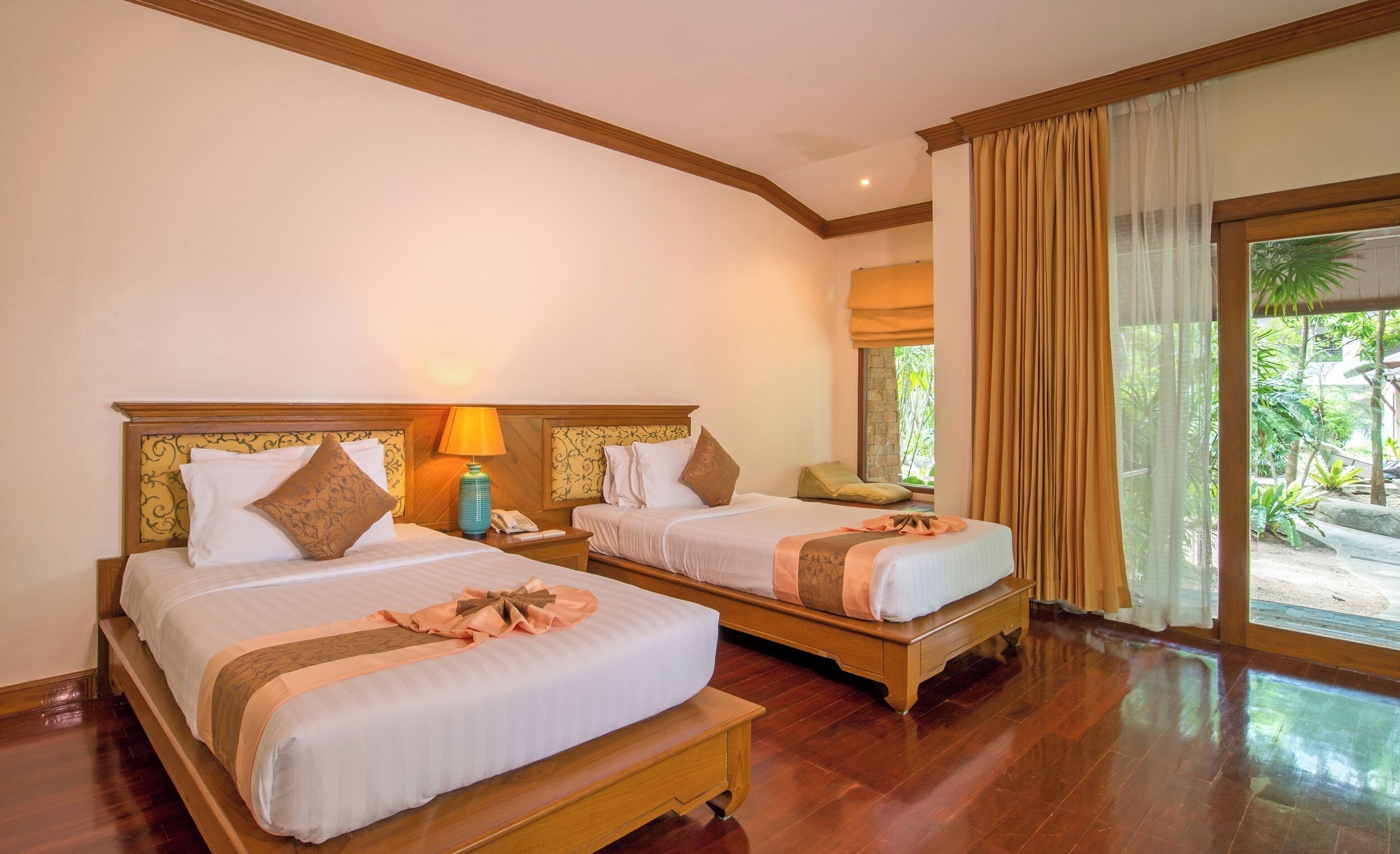 A hotel room with two beds, wooden headboards, and a large window with curtains.