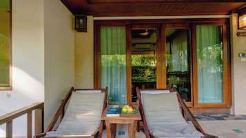 Eine Holzterrasse mit zwei Liegestühlen und einem Tisch, auf dem ein Buch und Obst liegen.