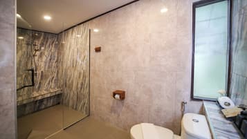 Een moderne badkamer met een glazen douchecabine, toilet en een betegelde muur van marmer.
