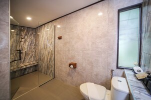 Een moderne badkamer met een glazen douchecabine, toilet en een betegelde muur van marmer.