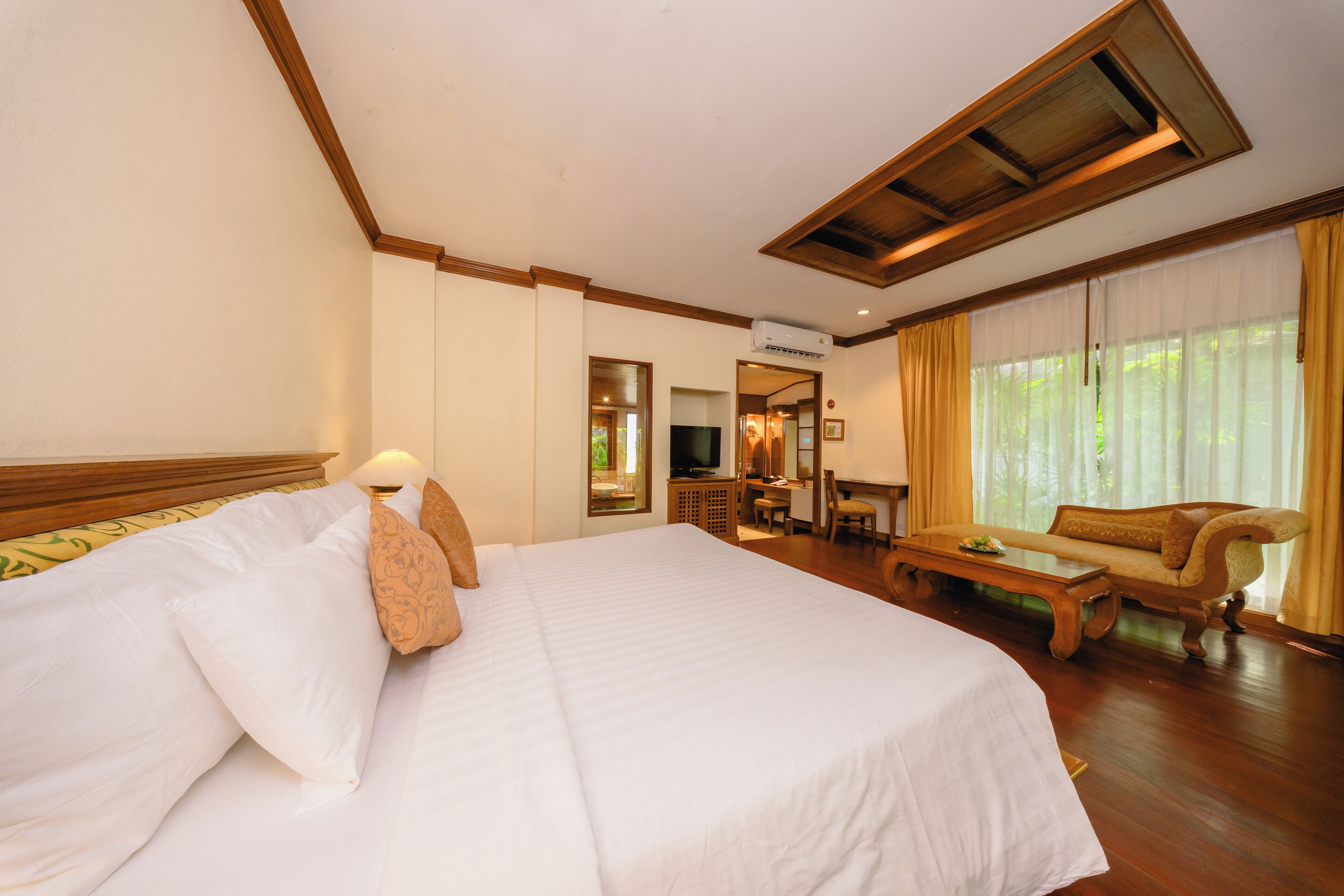 A hotel room with a large bed, a wooden headboard, a television, a sofa, and a desk.