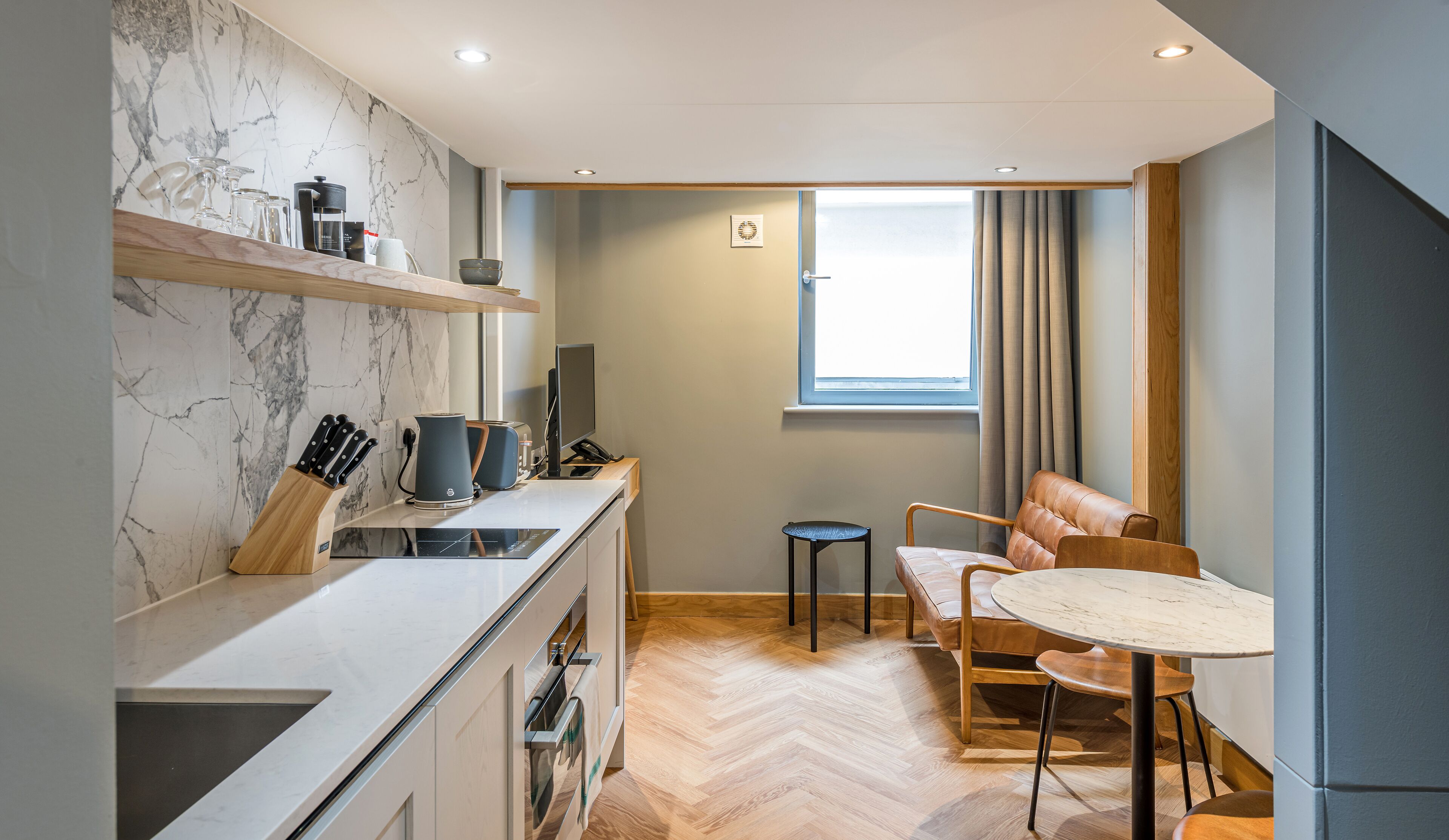 A compact kitchen with a marble backsplash, a dining area with a round table, and a window with curtains.