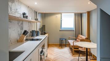 A compact kitchen with a marble backsplash, a dining area with a round table, and a window with curtains.