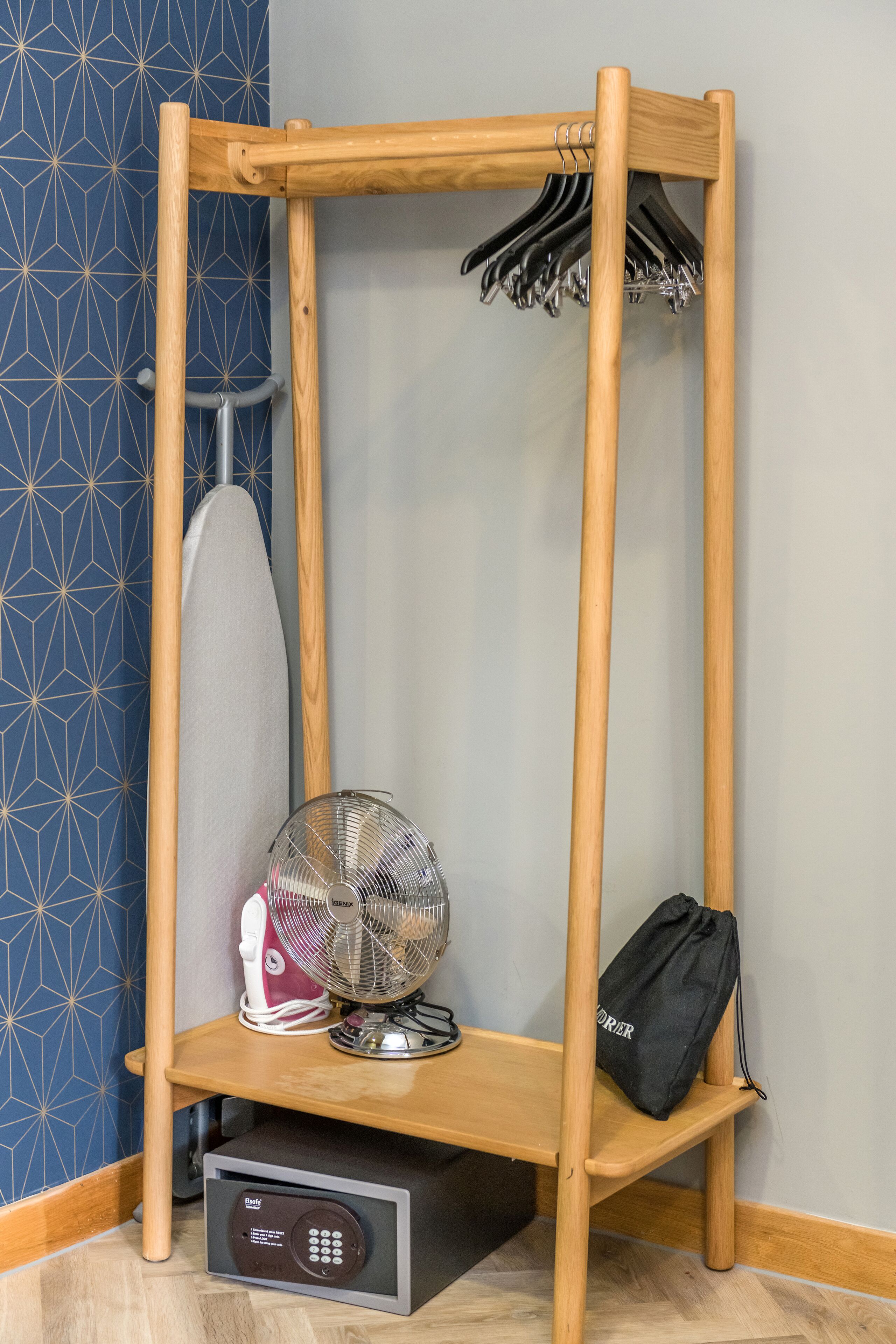 A wooden shelf with a hanging rack, a fan, a small appliance, and a bag.