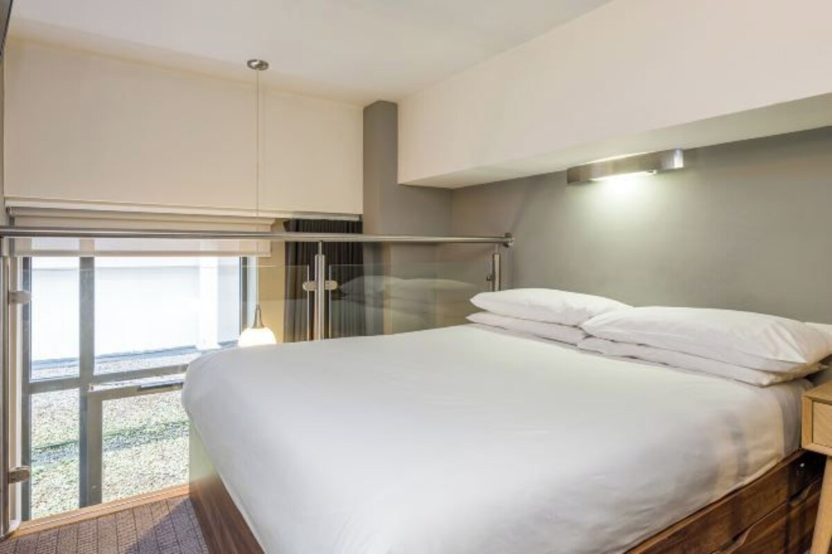 Ett modernt hotellrum med en stor säng, utsikt genom en glasdörr och ett litet sängbord.