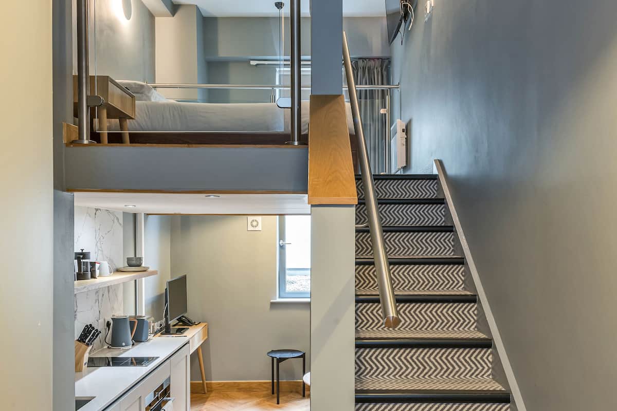 Un intérieur moderne avec un escalier menant à une chambre en mezzanine, un coin cuisine et un petit espace salon.